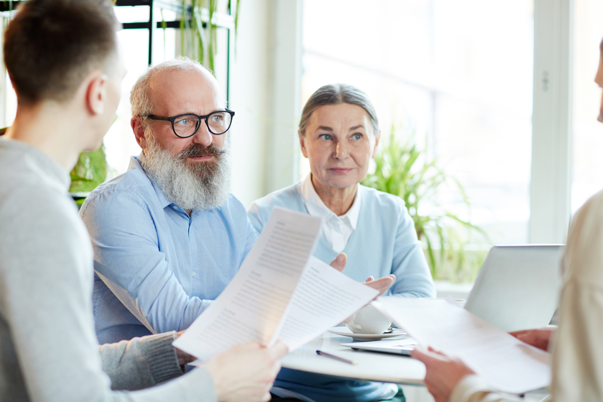 Adult children reading papers to senior couple