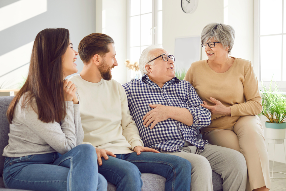 Adult children sitting on couch with senior parents smiling