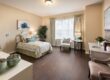 Clean bedroom with lots of space, a bed, 3 chairs, and a window