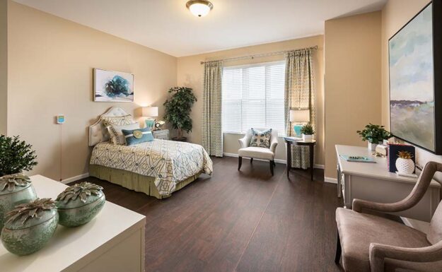 Senior Cottages vs. Independent Living Apartments Clean bedroom with lots of space, a bed, 3 chairs, and a window