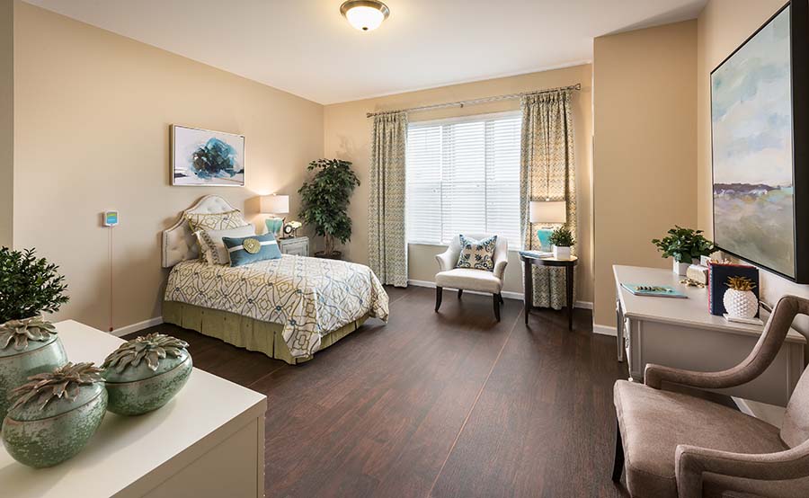 Senior Cottages vs. Independent Living Apartments Clean bedroom with lots of space, a bed, 3 chairs, and a window